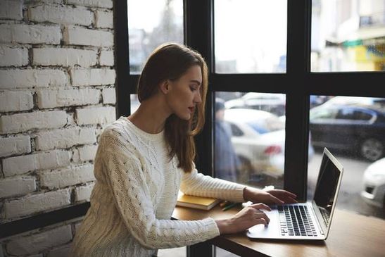 Woman composing a personalized cold email on a laptop at a coffee shop